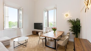 A modern dining area with a wooden table, six chairs, a TV, and a large window. - Rental in Rome Mellini View Apartment (Rome)