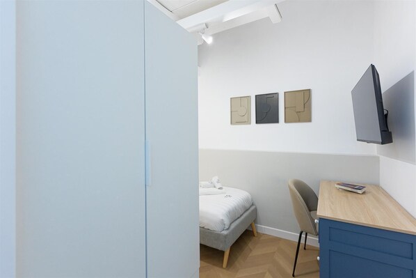 A bedroom with a bed, a desk, and a chair. There are three wall-mounted artworks and a television on the wall.
