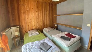 A room with wooden walls, two beds, a nightstand with a lamp, and a radiator. - CASA-Salon Bocca di Rosa suite pour 6 personnes (Molines-en-Queyras)