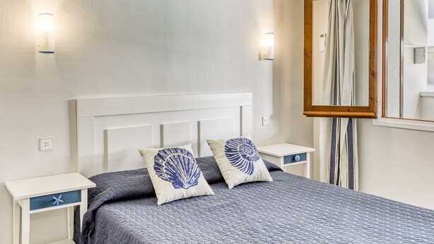 Een slaapkamer met een bed, nachtkastjes, een spiegel en wandlampen.