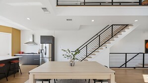 A modern kitchen with a central island, a stainless steel refrigerator, and a staircase leading to an upper level.