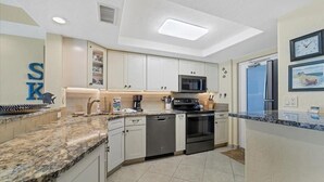 A modern kitchen with white cabinets, granite countertops, stainless steel appliances, and a built-in microwave.