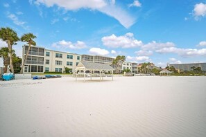 Un hotel frente a la playa con varios pisos, una zona de estar al aire libre techada y una playa en primer plano.