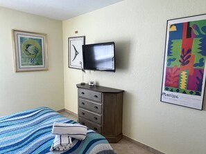 A bedroom with a bed, a dresser, a television, and artwork on the walls.