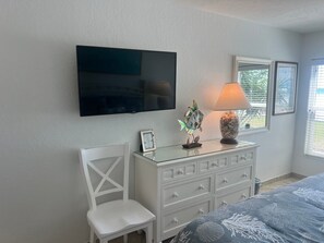 A bedroom with a bed, a dresser, a chair, a TV, and a window with blinds.