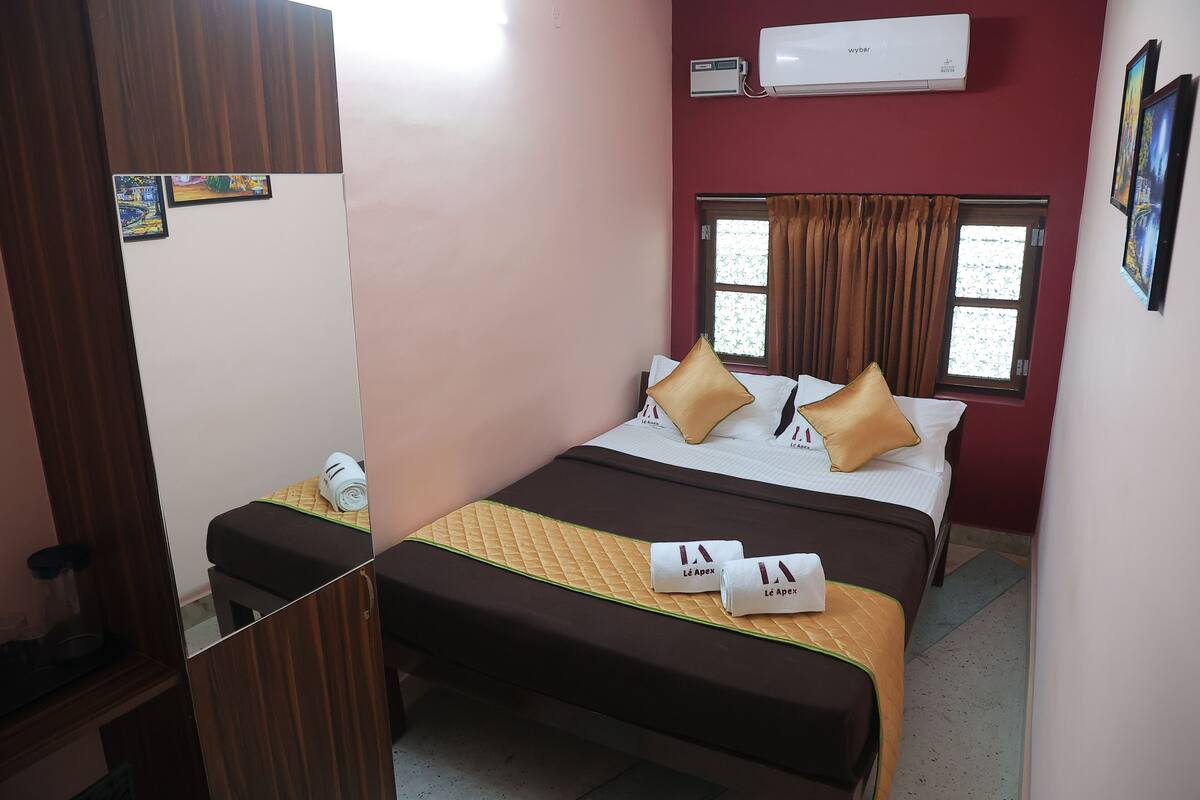 Quarto de hotel com cama, mesa de cabeceira, ar condicionado e janela com cortinas.