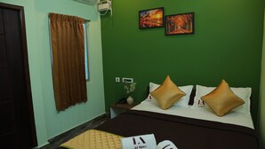 A hotel room with a bed, brown curtains, two paintings on the wall, and a small nightstand with a vase of flowers.
