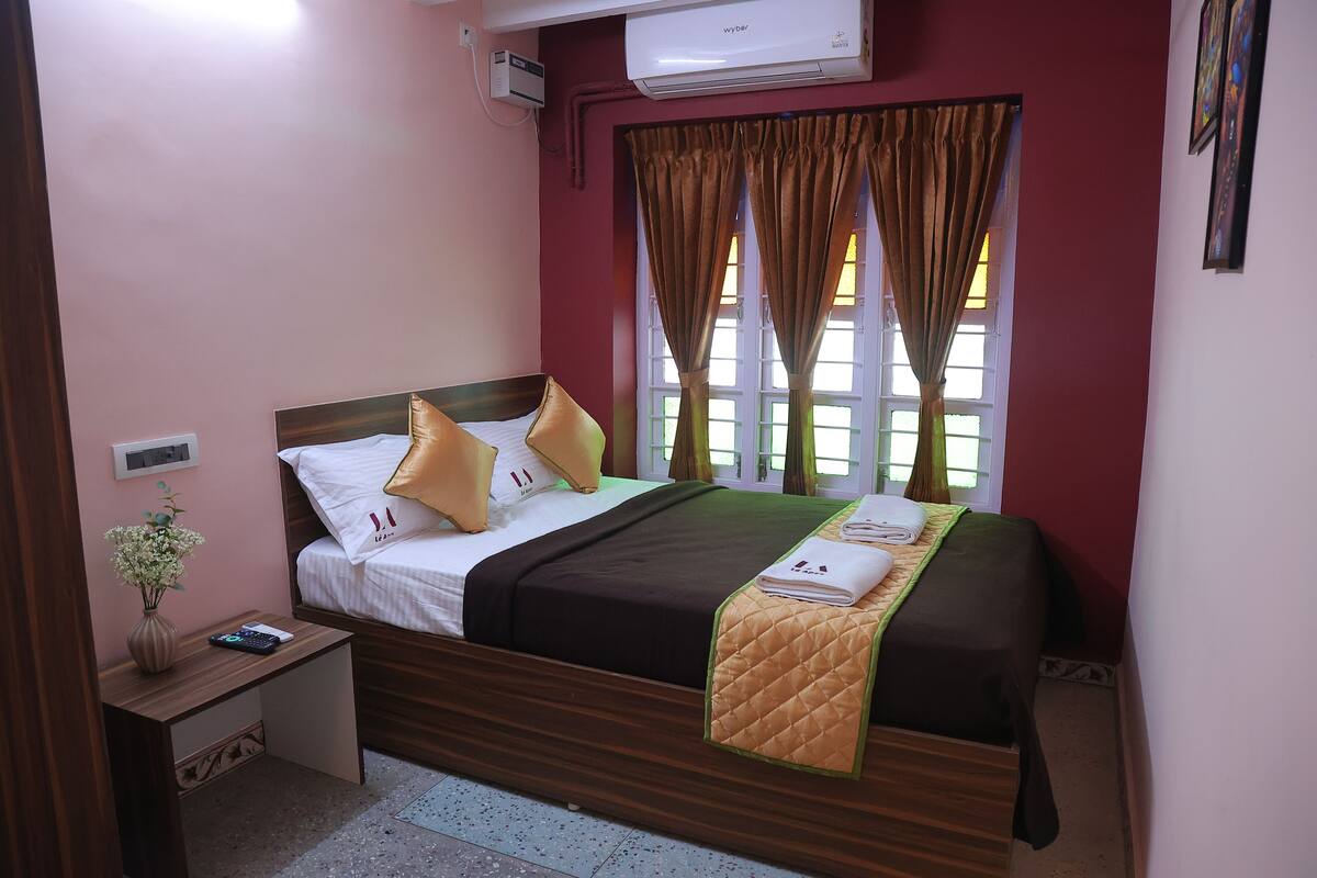 Quarto de hotel bem arrumado com cama, mesa de cabeceira e janela com cortinas.
