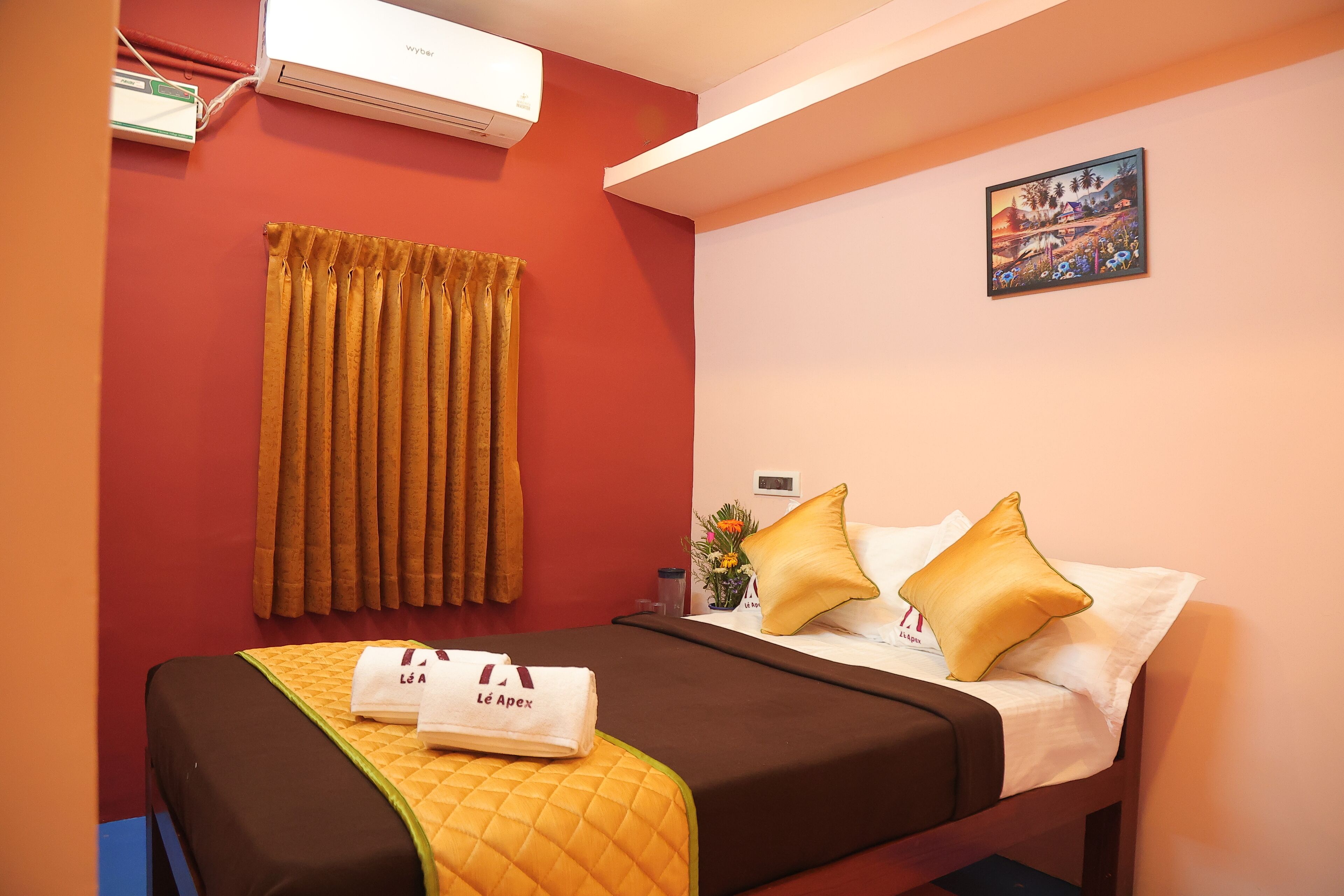 A hotel room with a bed, curtains, a painting, and an air conditioner.