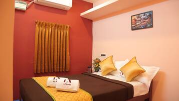 A hotel room with a bed, curtains, a painting, and an air conditioner.