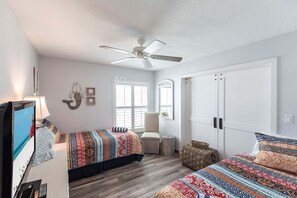 Une chambre à coucher comprenant un lit, une chaise, un ventilateur de plafond, une armoire et un téléviseur.