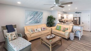 A living room with a beige sofa, a wicker armchair, a coffee table, and a ceiling fan.