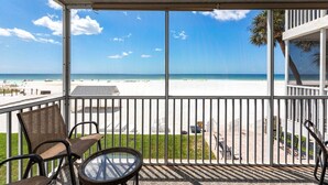A balcony with a view of a beach, chairs, and a table.