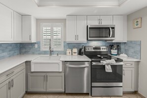A modern kitchen with stainless steel appliances, white cabinetry, and a blue-tiled backsplash.