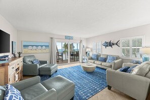 A spacious living room with a view of the ocean, a large flat-screen TV, and a dining area with a view of the patio.