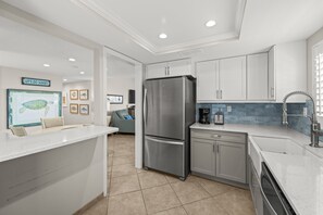 A modern kitchen with white cabinetry, a stainless steel refrigerator, and a coffee maker on the counter.