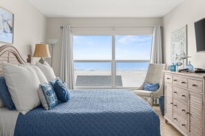 Un dormitorio con una cama grande, una silla, un aparador y vista a la playa.