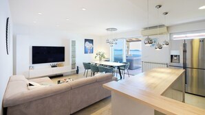 A modern kitchen with a central island, a dining area with green chairs, and a large flat-screen TV mounted on the wall. - Hedera Estate, Hedera A54 (Mlini)