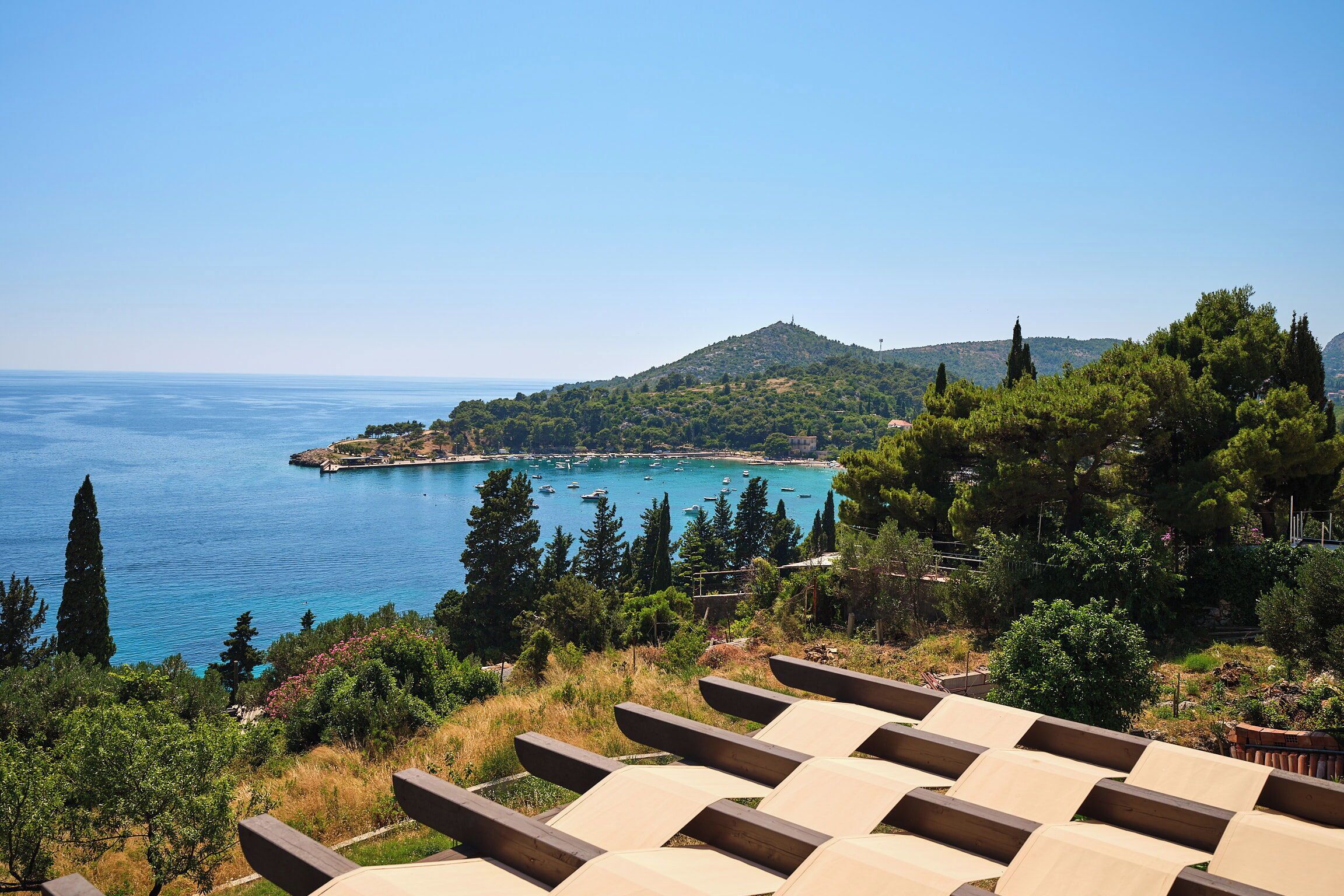 A coastal view with a chair area overlooking a bay with boats, surrounded by greenery and hills.