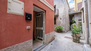 A narrow alleyway with a red building, a door, and a potted plant. - Apartment 'Casetta Bella' with Balcony, Wi-Fi and Air Conditioning (Condrò)