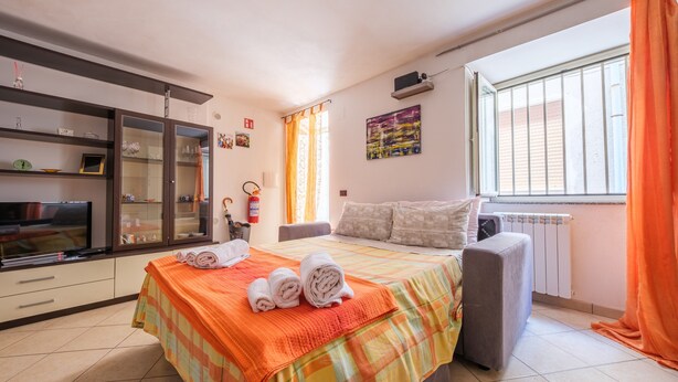 A bedroom with a bed, a TV, a radiator, and a window with curtains. - Apartment 'Casetta Bella' with Balcony, Wi-Fi and Air Conditioning (Condrò)