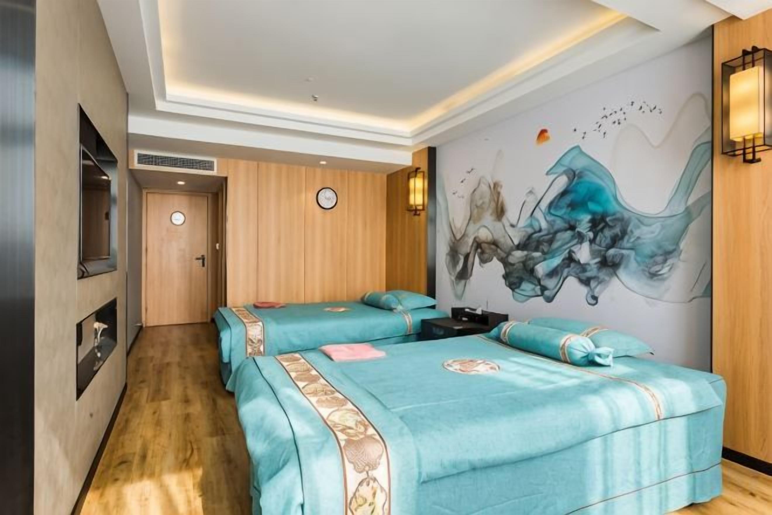 Une chambre d’hôtel avec deux lits, un plancher en bois, un mur orné d’un tableau et une horloge accrochée au mur.