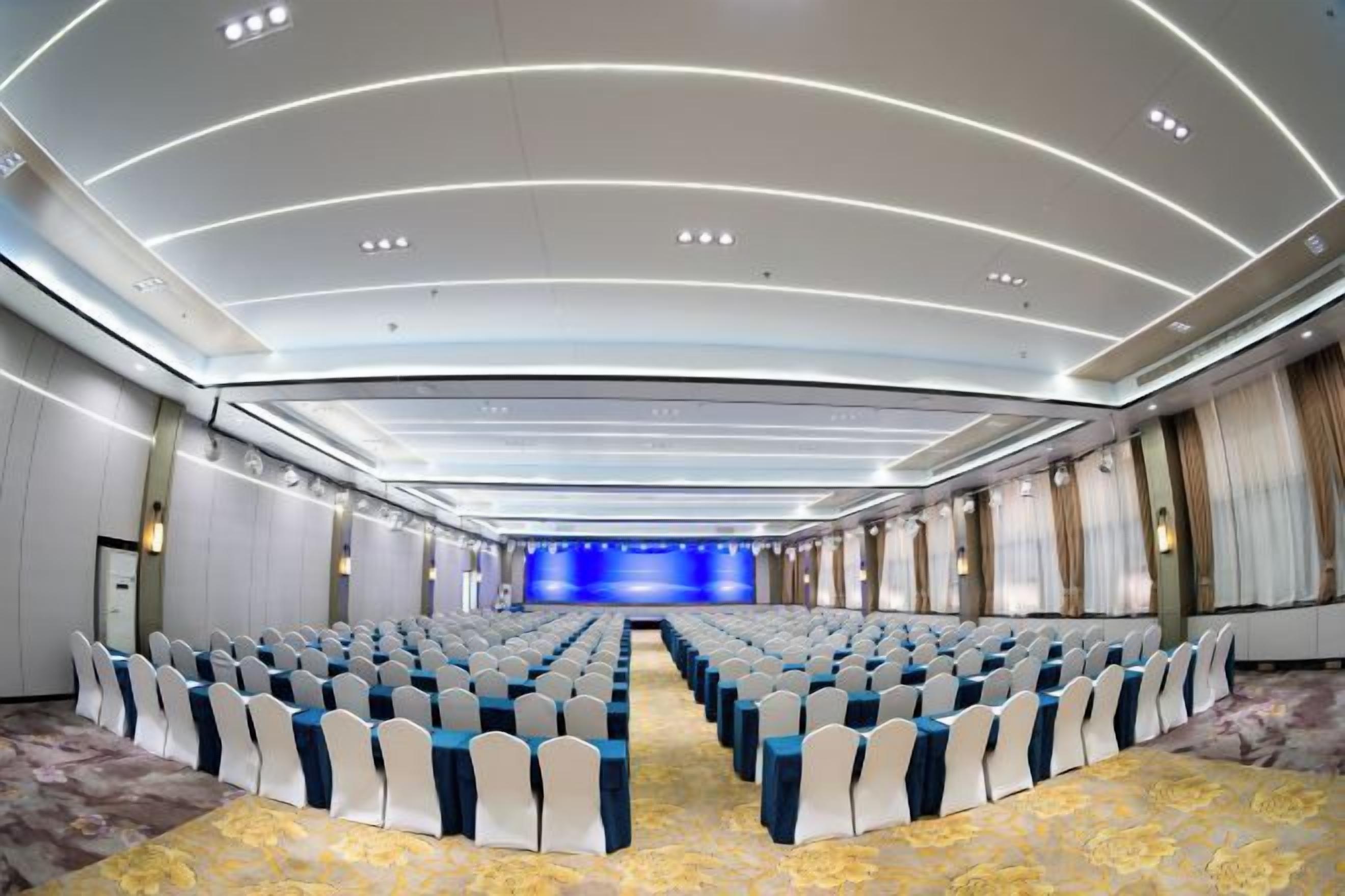 A conference room with rows of chairs, a stage, and a modern ceiling design.