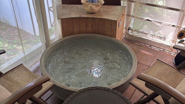 Een houten terras met een jacuzzi, een tafel en stoelen.