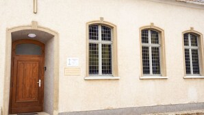 A building with a wooden door, a cross above it, and three arched windows. - Former church in new splendor (Oranienbaum-Wörlitz)