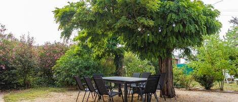 An outdoor dining area with a table and chairs, surrounded by trees and greenery.