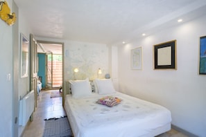 A bedroom with a bed, bedside lamps, a wall with artwork, and a door leading to another room.