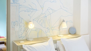 A hotel room with a bed, two bedside lamps, a wall with a blue line drawing, and a small table with a lamp. - Cocteau Guest Room with Shared Terrace, Wi-Fi, and Air Conditioning (Menton)