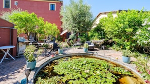 A courtyard with a pond, potted plants, outdoor furniture, and a red building. - Cocteau Guest Room with Shared Terrace, Wi-Fi, and Air Conditioning (Menton)