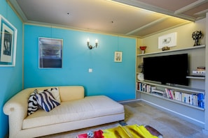 A living room with a sofa, a flat-screen TV, a bookshelf, and wall-mounted artwork.