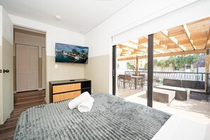 Una habitación de hotel moderna con una cama grande, un televisor de pantalla plana, un aparador de madera y un balcón con mobiliario exterior.