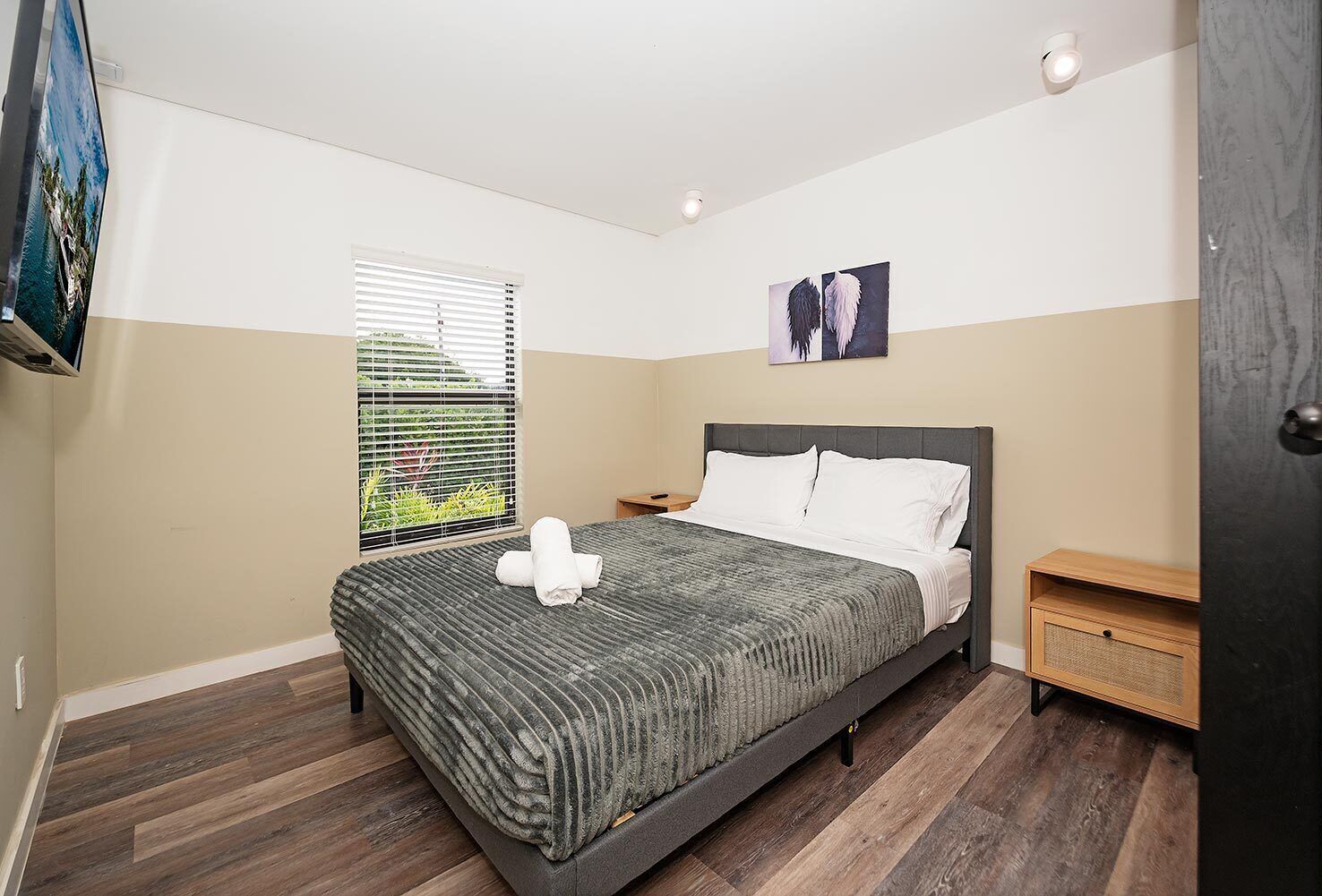 A bedroom with a bed, a nightstand, a window with blinds, and a painting on the wall.