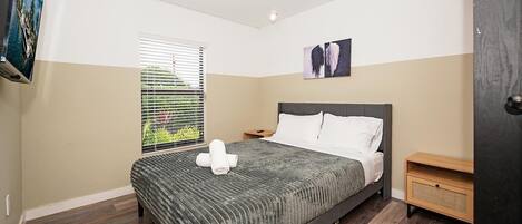 A bedroom with a bed, a nightstand, a window with blinds, and a painting on the wall.