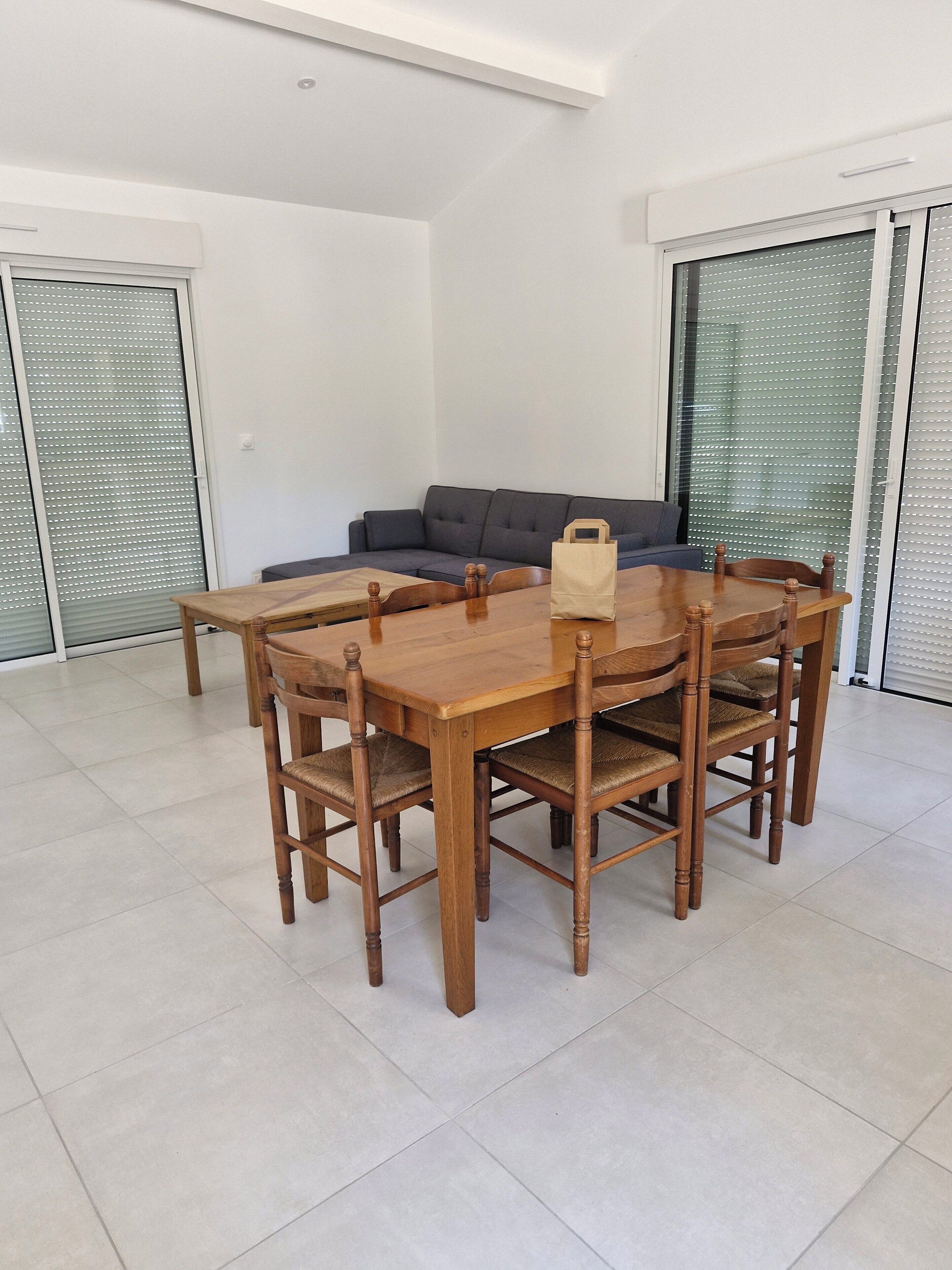 Un coin repas avec une table et des chaises en bois, un canapé gris et un sac posé sur la table.