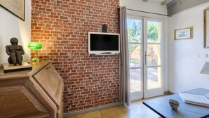 A room with a brick wall, a television mounted on it, a statue on a cabinet, and a door leading outside. - Grenade Guest Room with Shared Terrace, Wi-Fi, and Air Conditioning (Menton)