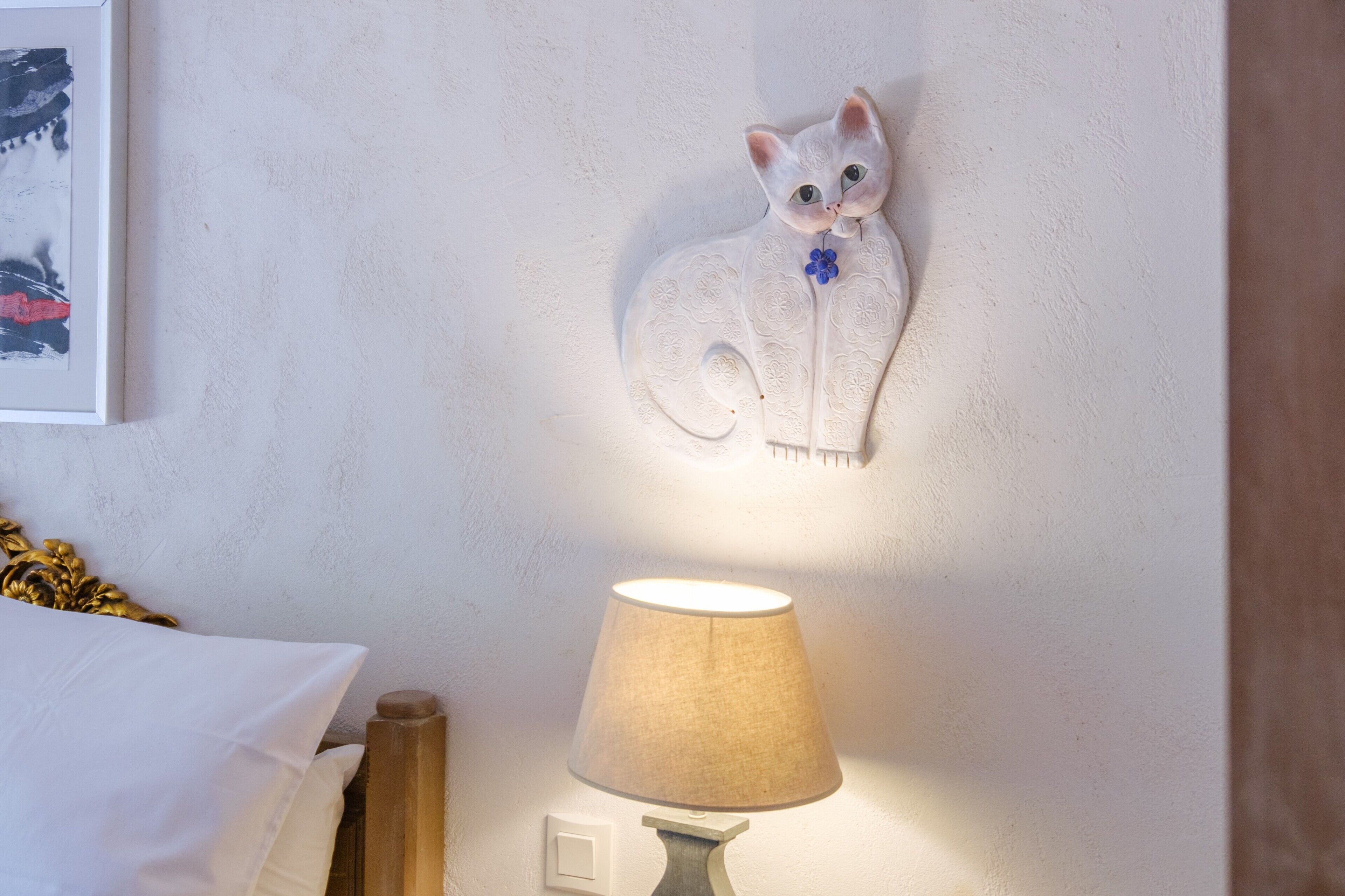A wall-mounted cat sculpture, a lamp, and a bed with white bedding.