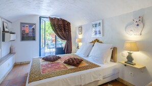 A bedroom with a bed, pillows, a bedside lamp, a window with curtains, and a wall-mounted cat decoration. - Grenade Guest Room with Shared Terrace, Wi-Fi, and Air Conditioning (Menton)