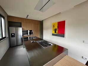 A modern kitchen with a stainless steel island, built-in appliances, and a red abstract painting on the wall.