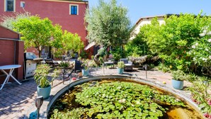 A courtyard with a pond, potted plants, outdoor furniture, and a red building. - Room 'Serena' with Shared Terrace, Wi-Fi, and Air Conditioning (Menton)