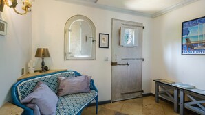 A room with a blue patterned sofa, a lamp, a door with a mirror, and a table with books. - Room 'Serena' with Shared Terrace, Wi-Fi, and Air Conditioning (Menton)