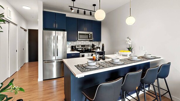 A modern kitchen with stainless steel appliances, a central island with bar stools, and pendant lighting.