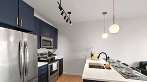A modern kitchen with dark cabinets, stainless steel appliances, a central island, and pendant lighting.