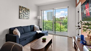 A modern living room with a dark blue sofa, a wooden coffee table, and a large window offering a city view.