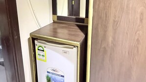 A compact refrigerator with a freezer compartment, a mirror above it, and a wooden cabinet to the right. - Wifaq Alnuzhah Hotel (Makkah)