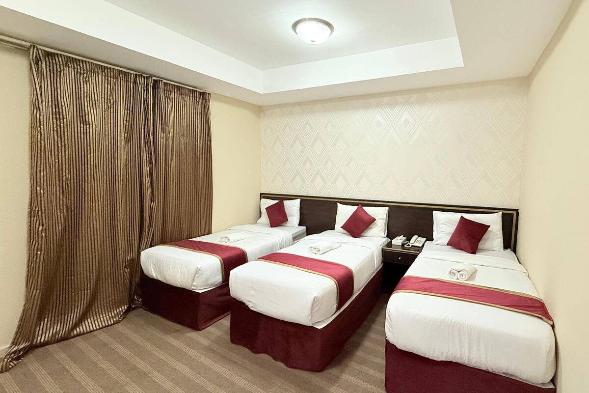 Une chambre d’hôtel avec deux lits simples, une grande fenêtre avec des rideaux, un mur décoré et un luminaire au plafond.