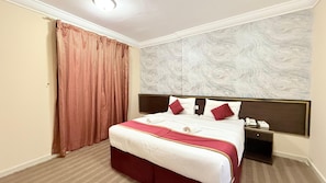 Une chambre d’hôtel avec un grand lit, une table de chevet, un téléphone et un mur décoré d’un motif imitant le marbre.